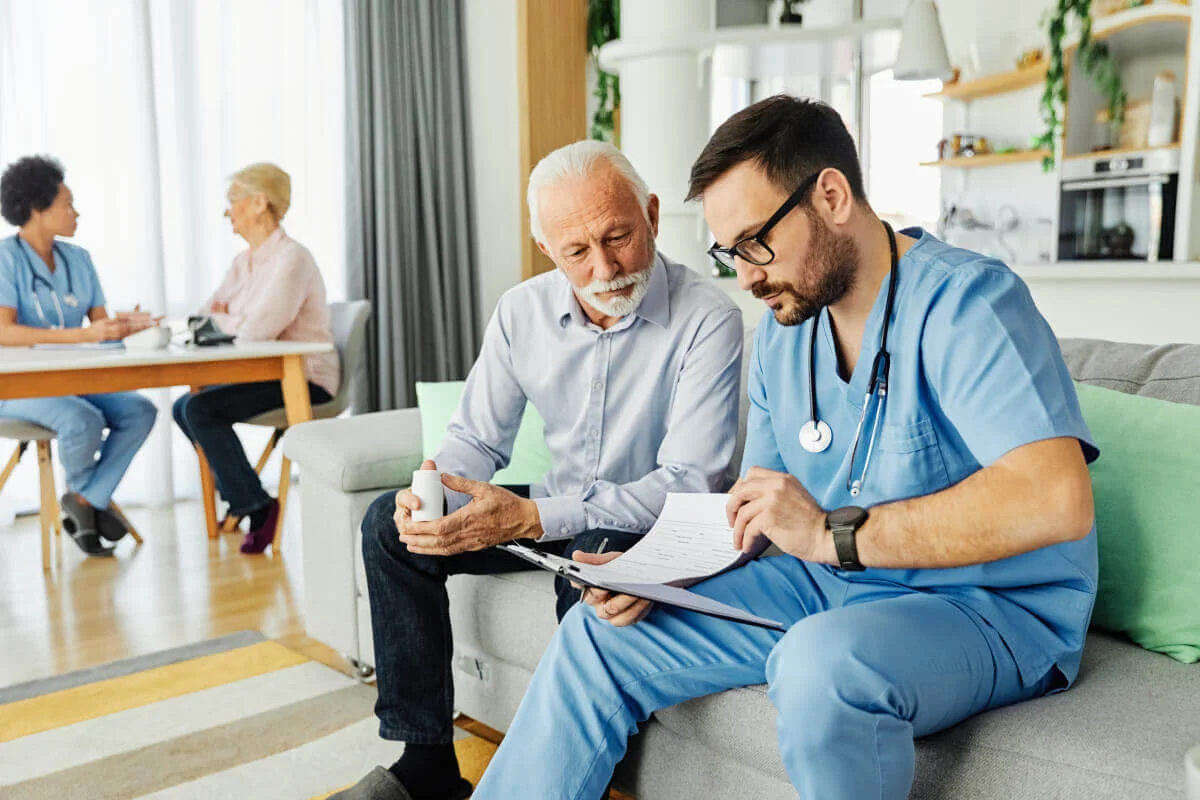 A nurse going over paperwork with an older man on a sofa