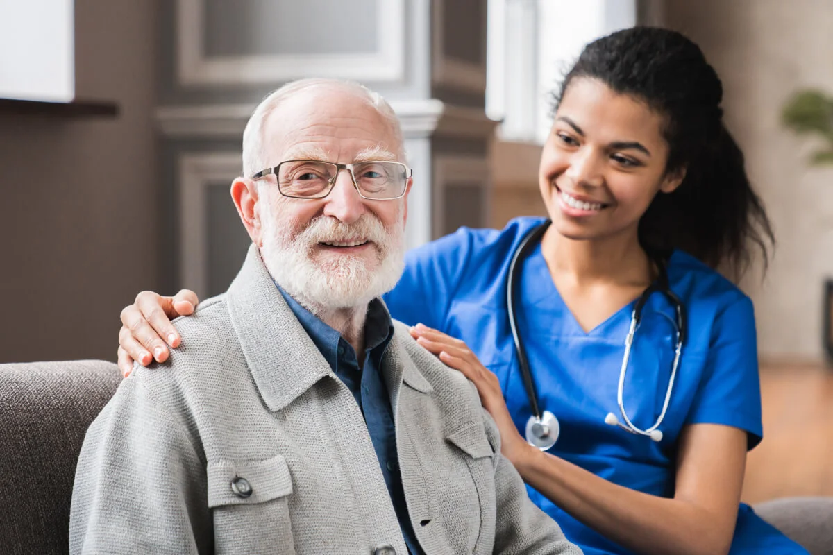 A smiling nurse with her hand on an older man's shoulder